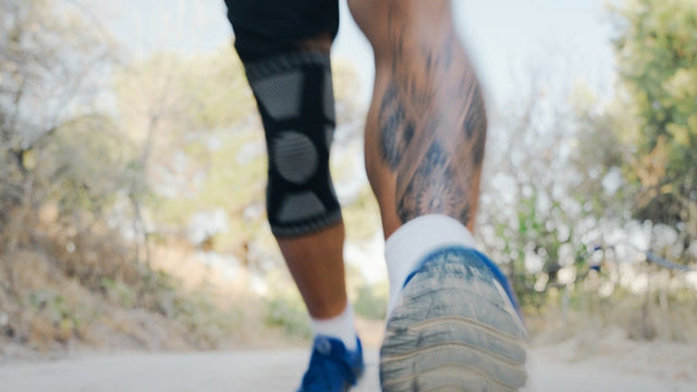Nahaufnahme von Beinen mit Kniebandage beim Laufen auf einem Schotterweg.