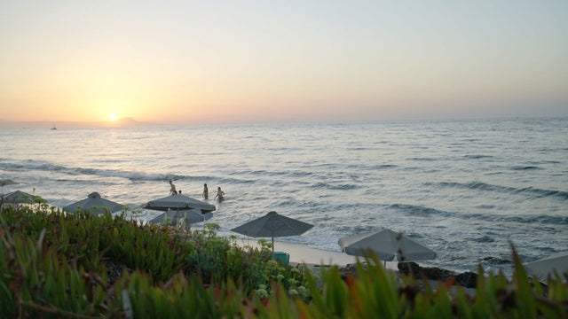 Sonnenuntergang über dem Meer, im Wasser sind einzelne Badende zu sehen.